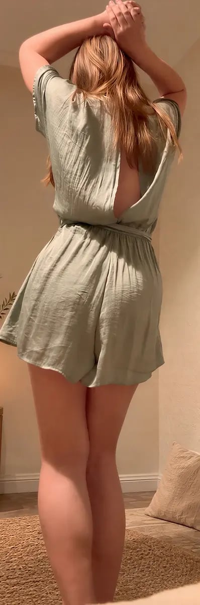 Tantra Melbourne, blonde woman seen from behind in an open back sage green playsuit with arms raised
